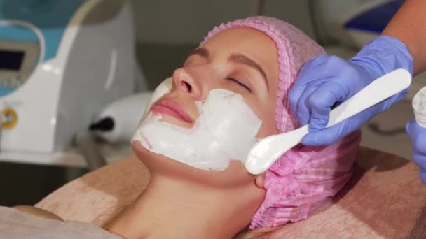 Happy woman smiling during facial mask application at beauty salon - Footage, Video