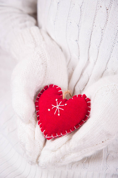 Mani in guanti bianchi a maglia che tengono il cuore decorativo rosso. Biglietto di San Valentino. Regalo romantico
 - Foto, immagini