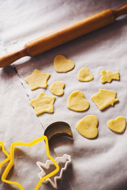 Dough in form of Christmas cookie (heart, star and house shaped) with rolling pin and metallic forms in daylight. Home bakery process. - Фото, изображение