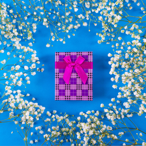 Violetti lahjapakkaus sydämen muotoinen ympäröi valkoinen gypsophila kukkia sinisellä pohjalla, ylhäältä. Kevät romanttinen lahja naisille
. - Valokuva, kuva