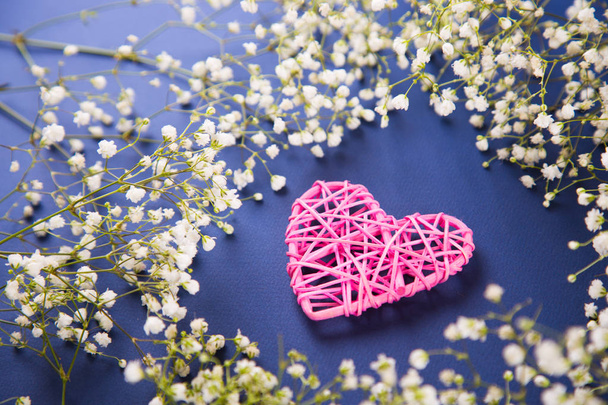 ピンクの枝編み細工品の心は暗い青色の背景は、高角度の白いカスミソウの花で囲まれています。春のロマンチックなカード. - 写真・画像