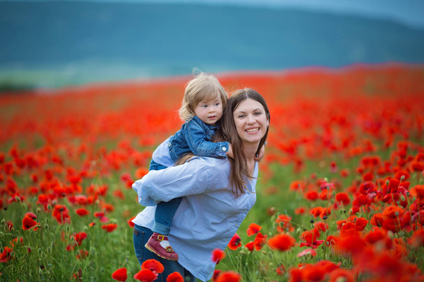 beautiful young woman with child girl in poppy field. happy family having fun in nature. outdoor portrait in poppies. mother with daughter. summer time. - Photo, image