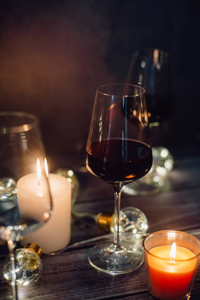 Holidays composition made of glass of red wine, candles and garlands on a dark background - Φωτογραφία, εικόνα