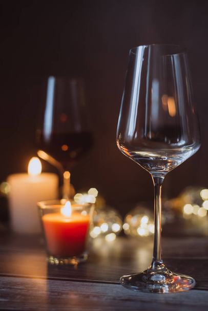Holidays composition made of glass of red wine, candles and garlands on a dark background - Фото, зображення