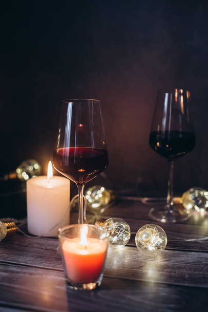 Holidays composition made of glass of red wine, candles and garlands on a dark background - 写真・画像