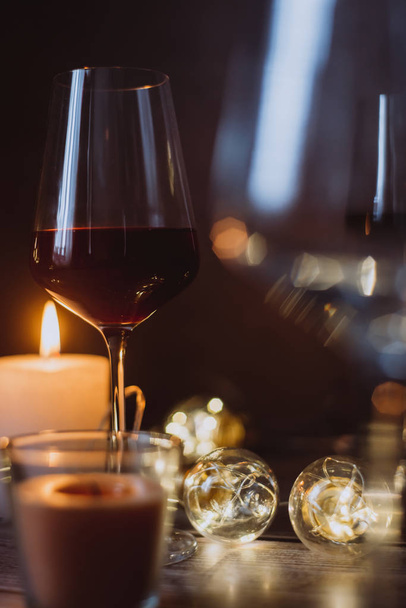 Holidays composition made of glass of red wine, candles and garlands on a dark background - Foto, Bild