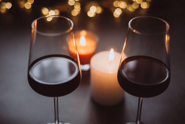 Two glasses of wine  red standing on a dark table with candle and  garlands - Foto, imagen