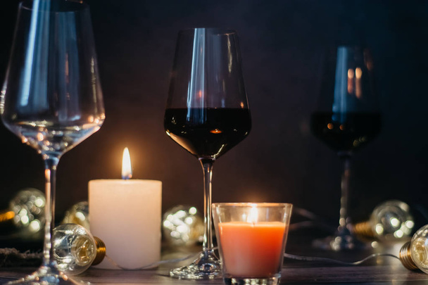 Holidays composition made of glass of red wine, candles and garlands on a dark background - Zdjęcie, obraz