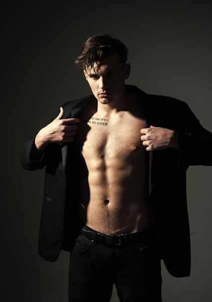 Fashion concept. Macho on pensive face, muscular figure, sportsman, bodybuilder. Guy looks confident and attractive. Man with torso, muscular macho with six packs, dressing jacket, dark background - Photo, image
