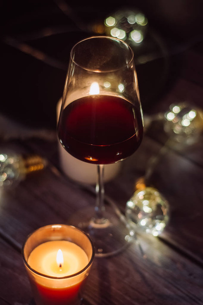 Holidays composition made of glass of red wine, candles and garlands on a dark background - Foto, imagen