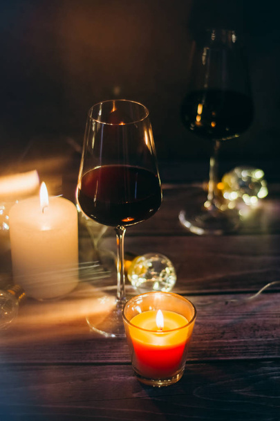 Holidays composition made of glass of red wine, candles and garlands on a dark background - Foto, imagen