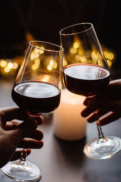 Two glasses of wine  red in hand on the background candle and  garlands  - Foto, Imagen