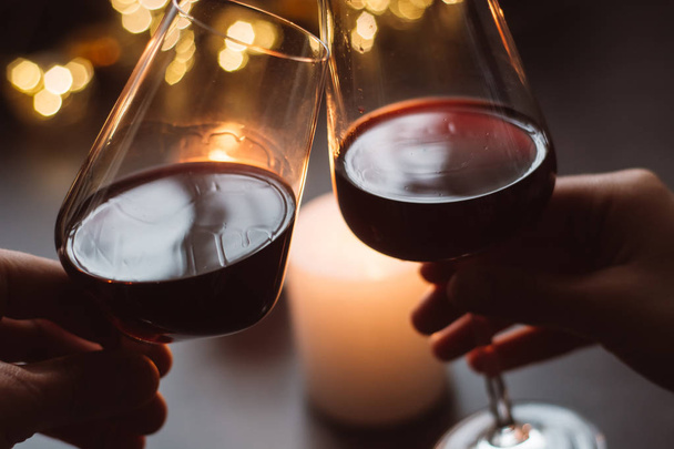 Two glasses of wine  red in hand on the background candle and  garlands  - Photo, image