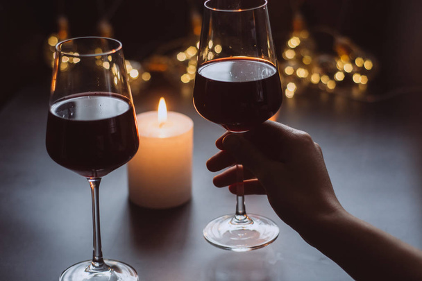 Two glasses of wine  red in hand on the background candle and  garlands  - Fotografie, Obrázek