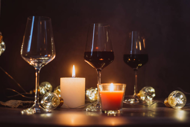 Holidays composition made of glass of red wine, candles and garlands on a dark background - Fotó, kép