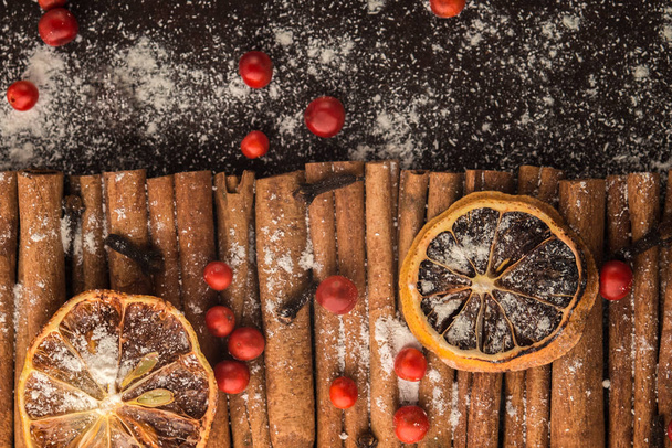 Christmas bakery and New Year concept. Holiday background with dried lemon citrus slices, set of cinnamon sticks and vanilla powder. Cosy winter holiday baking frame on dark background.  - Foto, Imagem