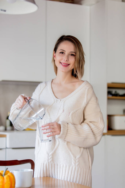 Young girl in sweater with glass of water at kitchen - Foto, imagen