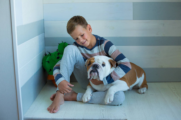 Handsome Young Boy wearing cozy pajamas Playing with His english funny bull Dog and enjoy life time weekend hanging each other with love and tender. Cactus toy. - Foto, Imagen
