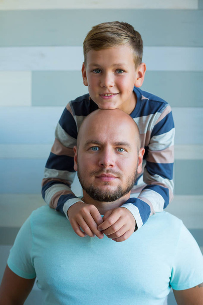Side view of handsome father and his cute son looking at each other and smiling while spending time together at home. Blue eyes and plenty blue color tones - Foto, afbeelding