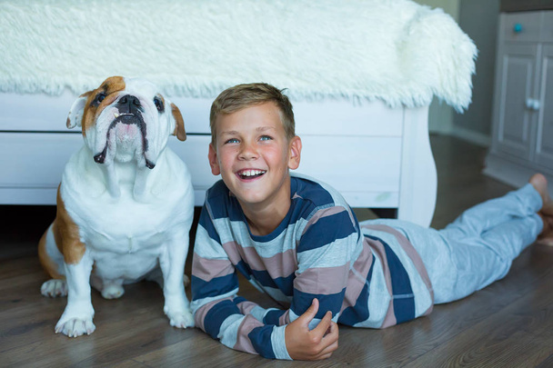 Handsome Young Boy kid wearing cozy pajamas Playing with His english funny bull Dog on the floor and enjoy life time weekend hanging each other with love tender. - Фото, зображення