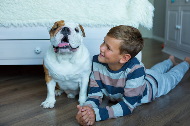 Handsome Young Boy kid wearing cozy pajamas Playing with His english funny bull Dog on the floor enjoy life time weekend hanging each other with love and tender. - Foto, immagini