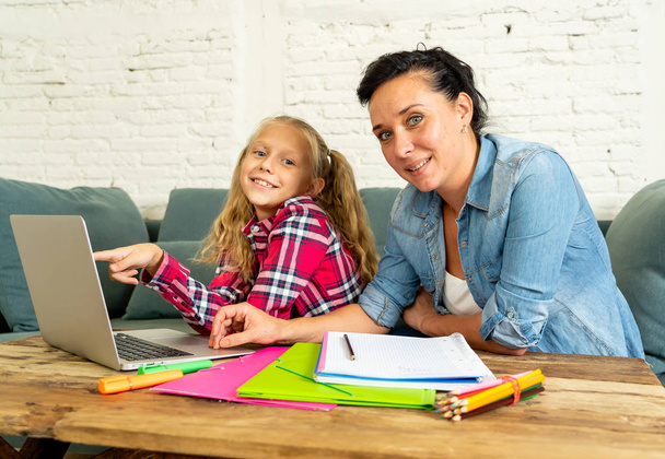 Mother helping young girl doing homework with laptop and school books sitting on the sofa at home in parenting homework and education concept - Foto, Imagen