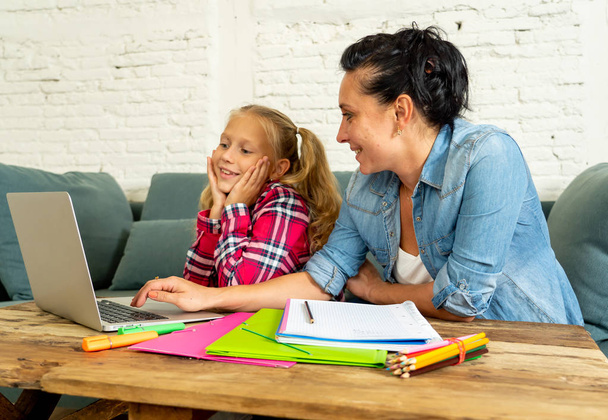 Mother helping young girl doing homework with laptop and school books sitting on the sofa at home in parenting homework and education concept - Foto, Bild