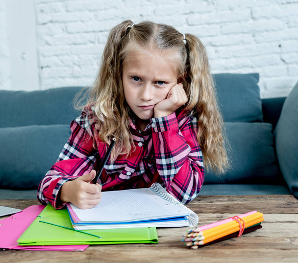 Cute sweet sad and overwhelmed blonde hair primary school girl looking angry bored and tired in stress with homework and studying with books and computer at home in children education concept. - Fotoğraf, Görsel