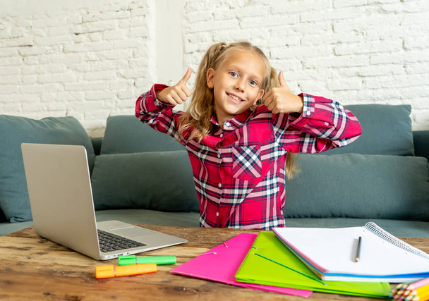 Cute caucasian cheerful elementary student feeling happy while doing homework and studying on her laptop in living room at home in new technology school education concept. - Фото, зображення
