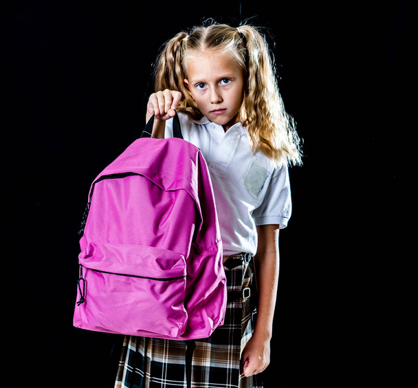 unhappy school girl holding a big schoolbag full of books and homework isolated on black background in back to school learning difficulties homework and education concept. - Photo, Image