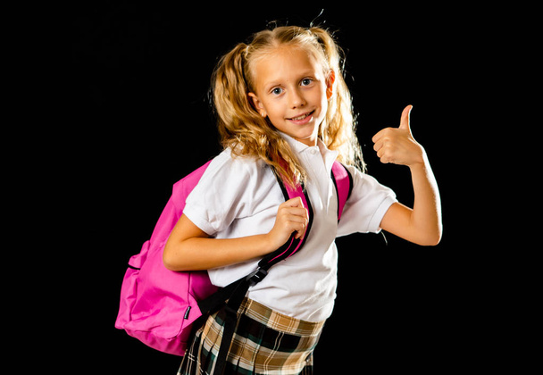 Pretty cute blonde hair girl with a pink schoolbag looking at camera showing thumb up gesture happy to go to school isolated on black background in back to school and children education concept. - Foto, imagen