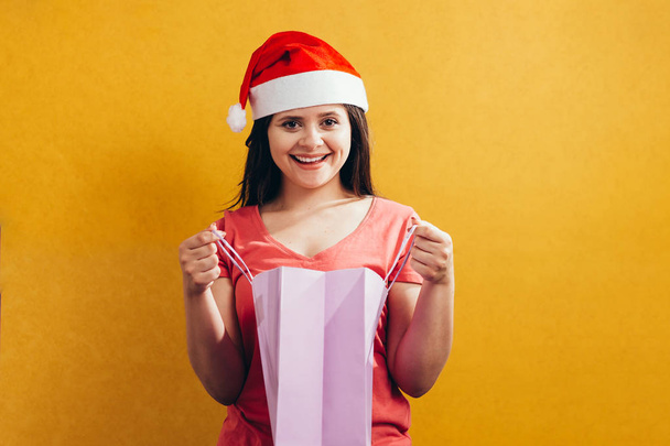 Beautiful woman with a santa hat holding shopping bags on color background - Photo, Image
