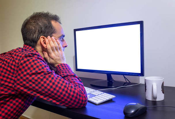 Surprised Man Stares at Office Computer on Wooden Black Desk Mockup. Dotted Red Shirt, LCD Screen, Keyboard, Mouse, White Mug. Copy Space. - Photo, Image