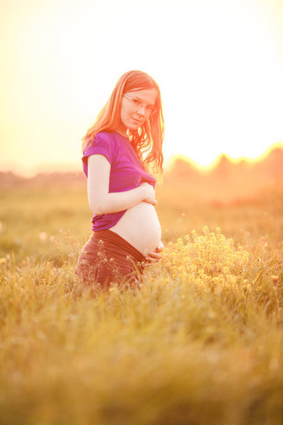 Femme enceinte sur fond de coucher de soleil et de nature. Belle jeune fille modèle avec ventre au soleil, dans le rétroéclairage
. - Photo, image