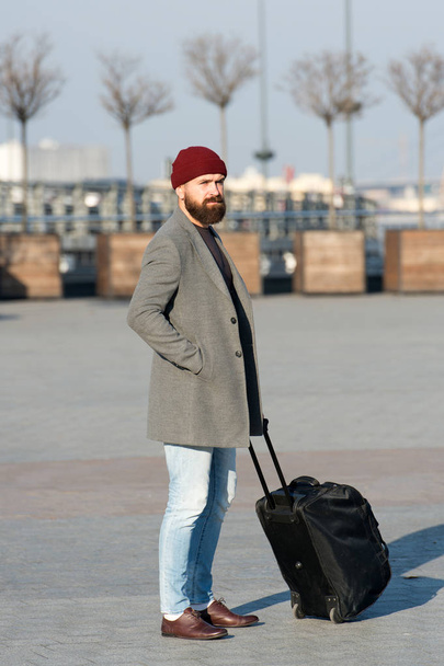 Férfi szakállas hipszter utazás nagy bőrönddel a kerekeken. Kezdődjön az utazás. Utazó bőrönddel, aki a reptéri vasútállomásra vár. Indulásra kész. Vidd az utazótáskát. Üzleti út - Fotó, kép