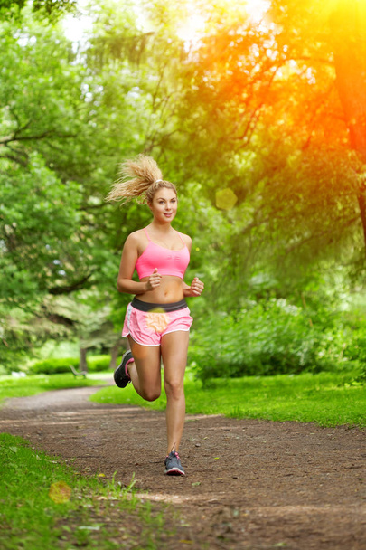 Young woman sports, running in the park. Girl model runs at sunrise or sunset outdoors. Healthy lifestyle, jogging. - Foto, imagen