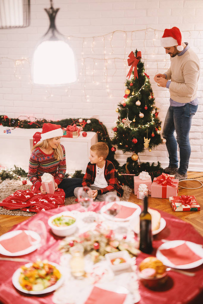 young happy parents and their adorable little son celebrating Christmas at home and decorating Christmas tree - Foto, Imagen