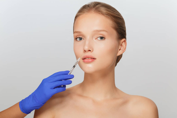 Portrait of young attractive lady getting beauty injection with syringe thoughtfully looking in camera over gray background - Valokuva, kuva