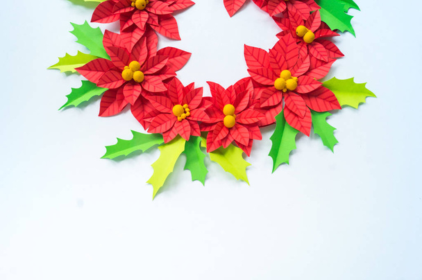 Paper flower poinsettia and leaves of holly. Christmas wreath. White background. Colors are green, red, yellow. - Фото, зображення