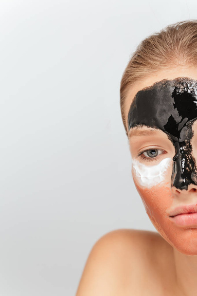 Κλείστε τη μισή γυναίκα αναστατωμένος με διαφορετικές καλλυντικά μάσκες στο πρόσωπο δυστυχώς αναζητούν στην άκρη πάνω από το γκρίζο φόντο - Φωτογραφία, εικόνα