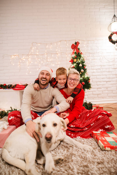 joven feliz familia celebrando la Navidad sentado en el suelo en casa con adorable perro Labrador Retriever
 - Foto, Imagen