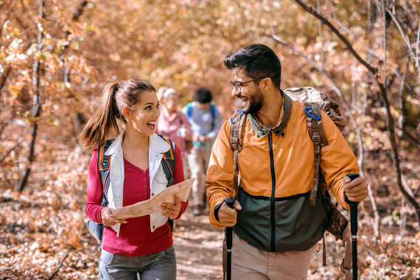 Group of hikers exploring the woods. Woman holding map, man smiling and talking to her, backpacks on backs. - Photo, Image