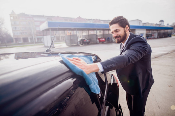 Hombre de negocios satisfecho puliendo su coche caro en frente de lavado de coches
. - Foto, imagen