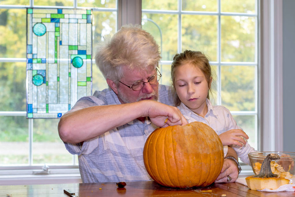 Dziadek i córka grand miarka się do wnętrza pomarańczowy dyni na Halloween dekoracji - Zdjęcie, obraz