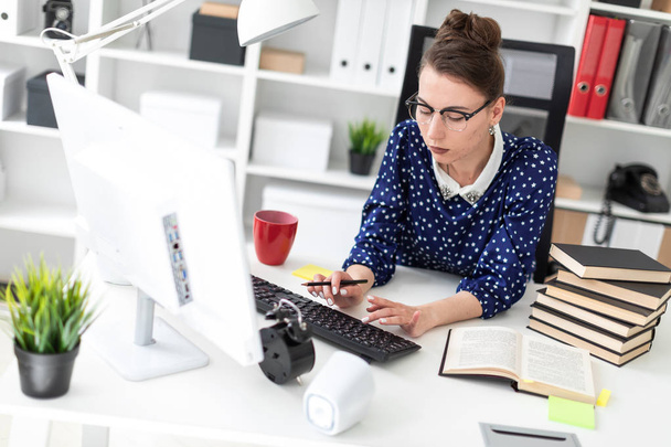 ein junges Mädchen mit Brille sitzt im Büro am Tisch und druckt auf der Tastatur. - Foto, Bild