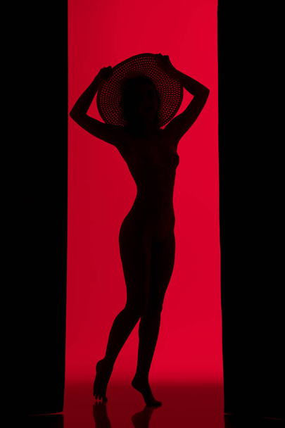 Girl in a hat silhouette view against red wall - 写真・画像