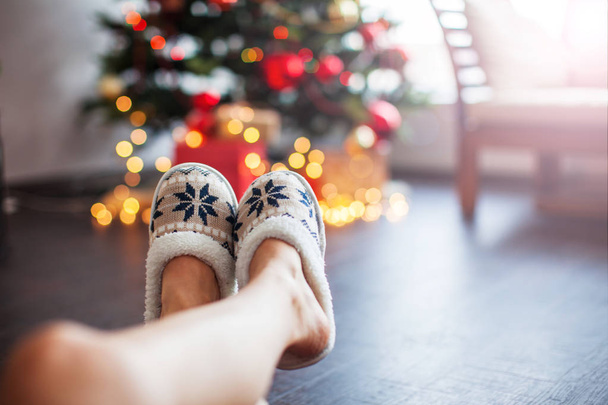 Legs in slippers on Christmas tree background. Comfort home textiles  - Fotó, kép