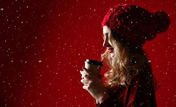 Pretty brunette woman in warm clothes drinking hot chocolate or coffee on red - Фото, зображення