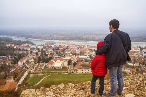 Mężczyzna i dziecko patrzeć na miasto, stojąc na szczycie wzgórza i patrzy w dół doliny. na horyzoncie jest widoczny z miasta. - Zdjęcie, obraz