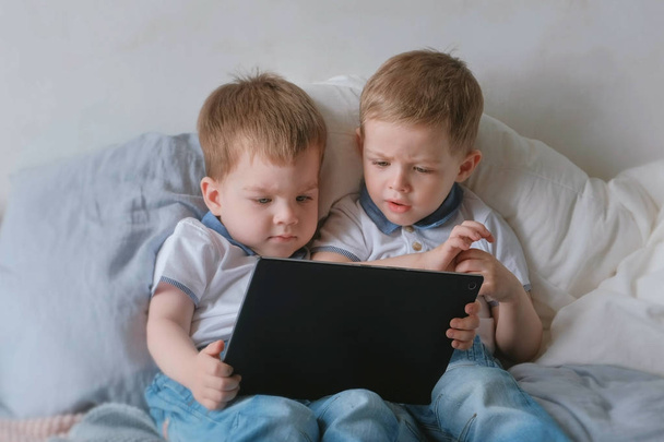 Kids with tablet. Two boys twins toddlers looking cartoon at tablet lying on the bed. - Valokuva, kuva